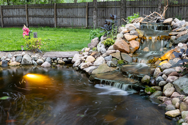 Backyard pond waterfall with rocks and underwater light on natural outdoor background