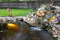 Backyard pond waterfall with rocks and underwater light on natural outdoor background